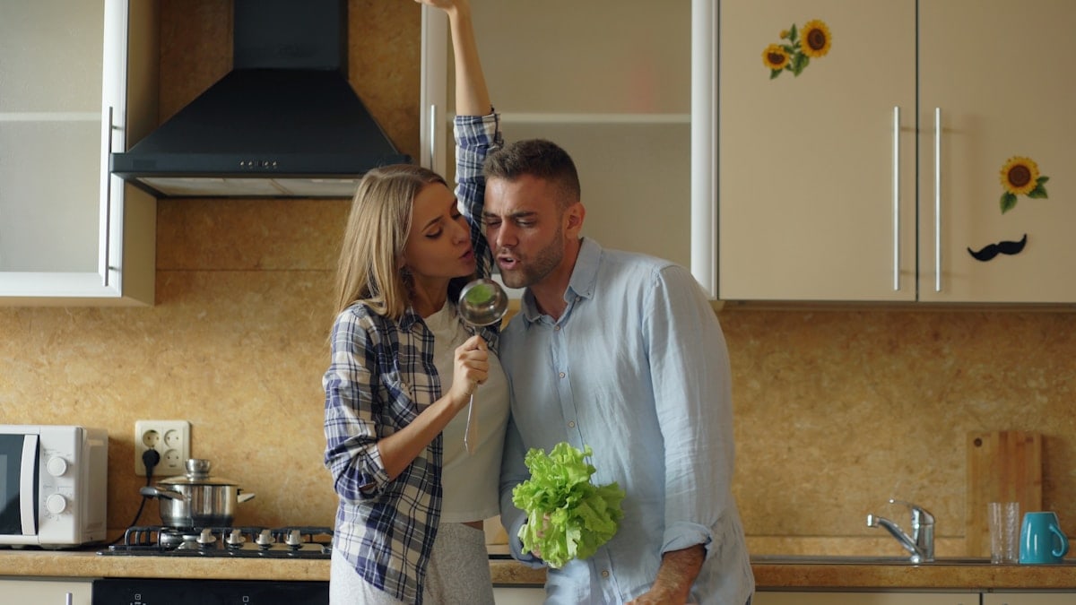 Attractive young joyful couple have fun dancing and singing while cooking in the kitchen at home in the morining